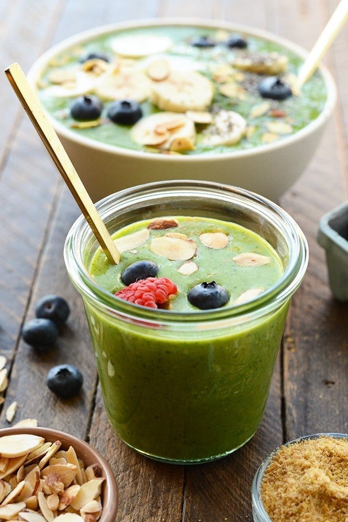 healthy green smoothie in a glass topped with berries and nuts