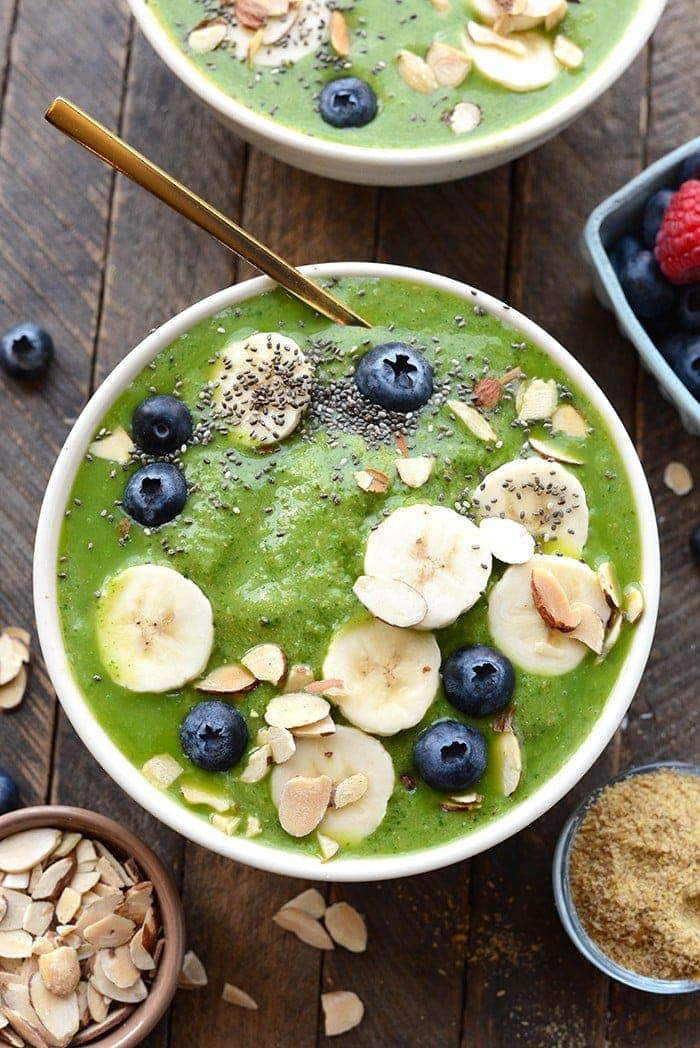 healthy green smoothie bowl topped with fruit and nuts