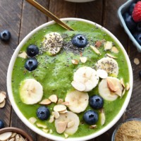 a bowl of green smoothie with berries and almonds.