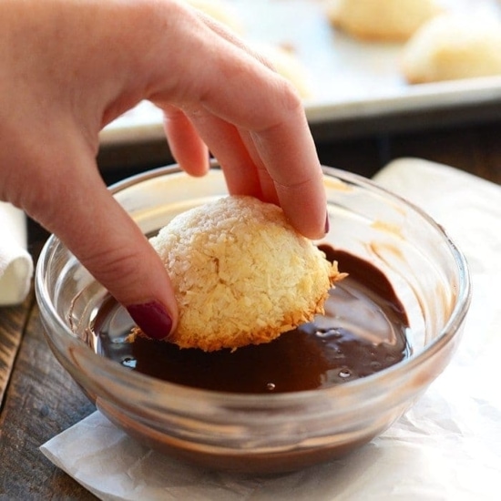 A person enjoying Coconut Macaroons by dipping them into chocolate sauce.