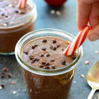 A person carefully pours a delicious chocolate peppermint chia seed pudding into a jar, garnishing it with candy canes.