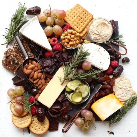 A holiday charcuterie board featuring a selection of cheeses, nuts, crackers, and grapes.