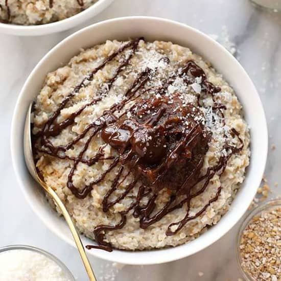 A bowl of oatmeal with chocolate sauce and granola.