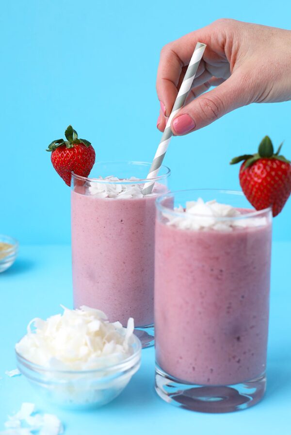 Two Coconut milk protein shakes in glass cups topped with coconut shavings and strawberries