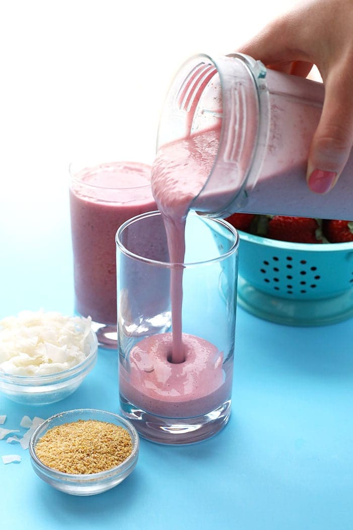 Hand pouring post-workout coconut strawberry smoothie from blender to glass 