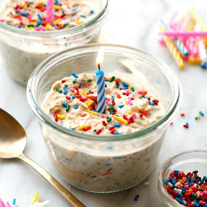 A birthday cake in a jar with sprinkles and a candle made from cake batter overnight oats.