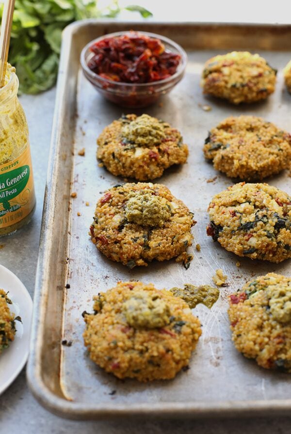 Quinoa patties displayed on a baking sheet accompanied by a jar of pesto.