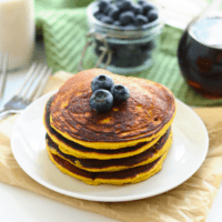 A stack of pumpkin pancakes with blueberries on a plate.