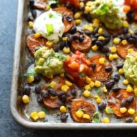 Mexican nachos on a baking sheet with guacamole and sour cream.
