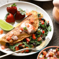 A plate of omelet with black beans, strawberries and salsa.