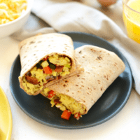 A breakfast burrito with eggs and vegetables on a plate.