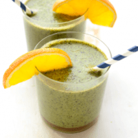 Two glasses of green smoothie with orange slices.