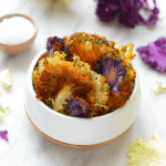 Cauliflower florets in a bowl with purple flowers.