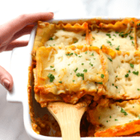Lasagna in a white dish with a wooden spoon.