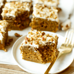 A slice of carrot cake on a plate with a gold fork.