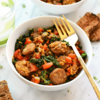 A bowl of kale and sausage with bread and a gold fork.