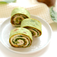 Three spinach and chicken wraps on a plate.