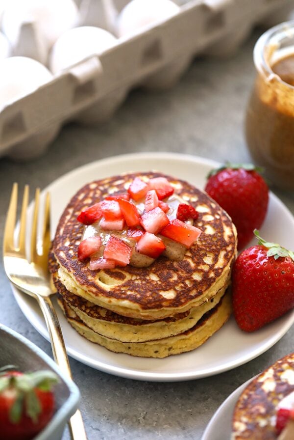 a plate of almond flour pancakes topped with strawberries and peanut butter.