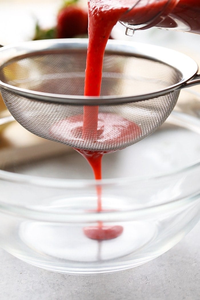 strawberry puree being strained through a sieve