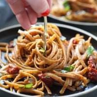 A person holding a fork on a plate of Sun Dried Tomato Basil Pasta.