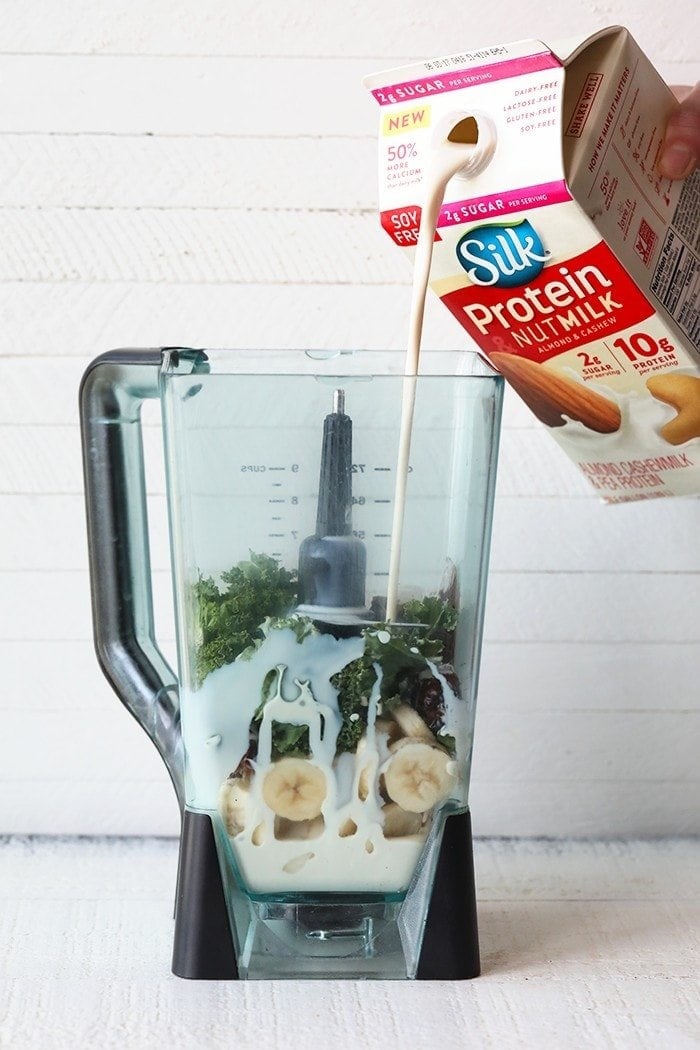pouring silk nut milk into blender with a banana date smoothie