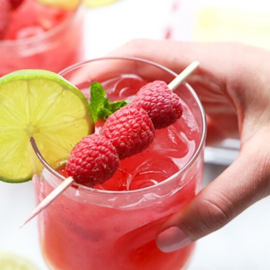 A person holding a raspberry mojito garnished with lime.