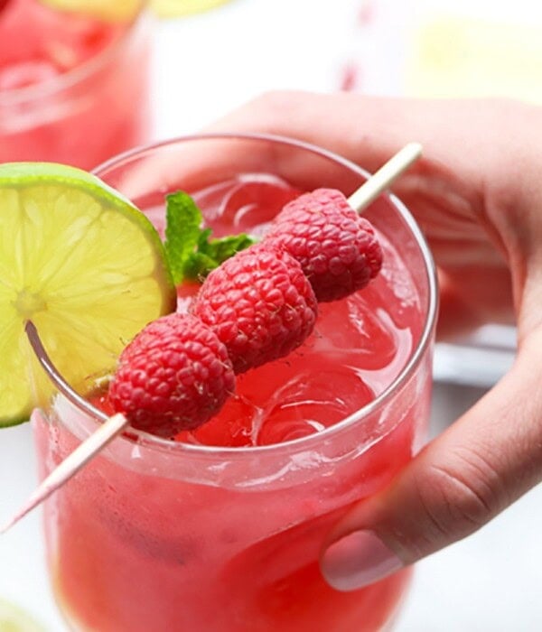 A person holding a raspberry mojito garnished with lime.
