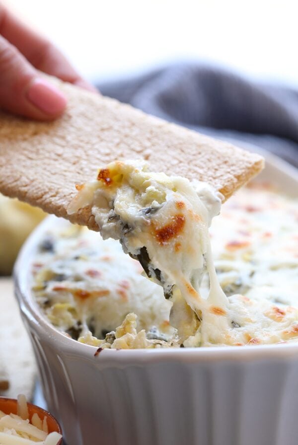 a person is dipping a cracker into a bowl of Lightened Up Spinach dip.