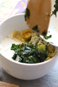 a bowl full of greens and cheese in a white bowl, Lightened Up Spinach and Artichoke Dip.