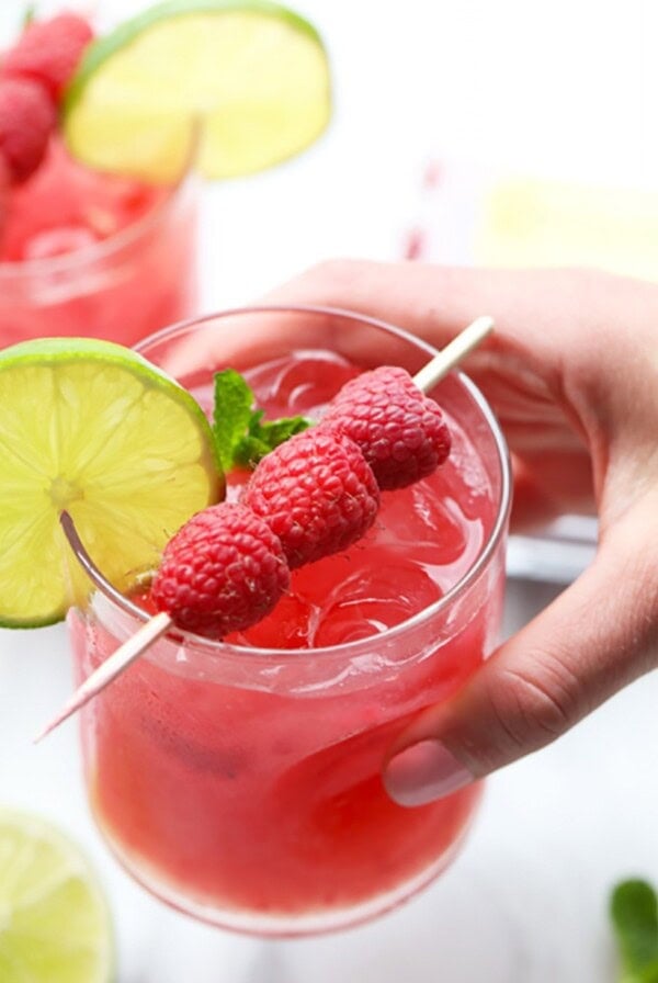 A person holding a raspberry ginger mojito garnished with lime.
