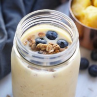 Breakfast in a jar with blueberries and granola, accompanied by a ginger pineapple smoothie.