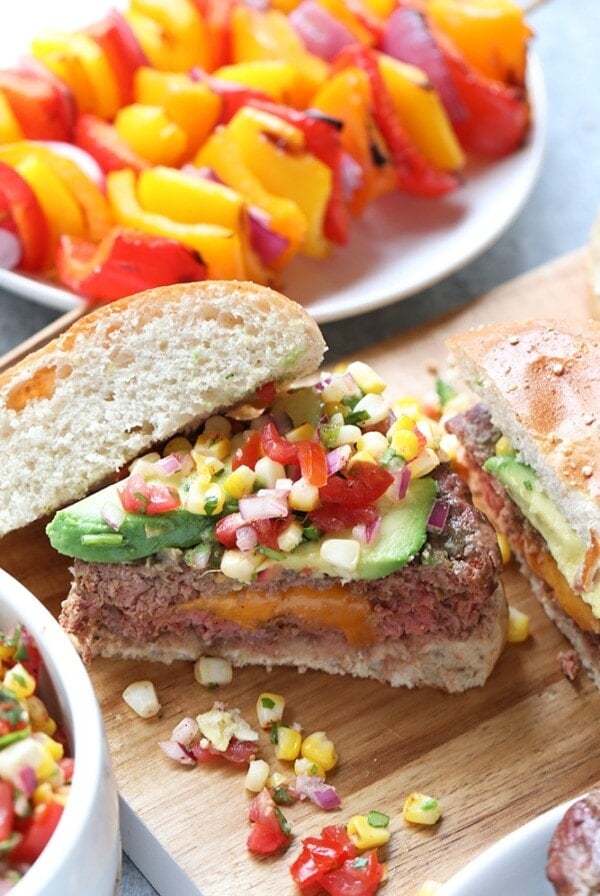 A cutting board featuring Mexican juicy lucys with burgers and vegetables.