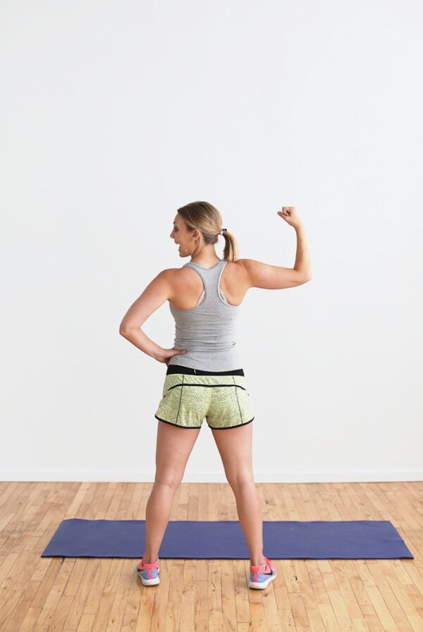 A woman flexing her arms in an empty room, showcasing her strength without the need for a gym.