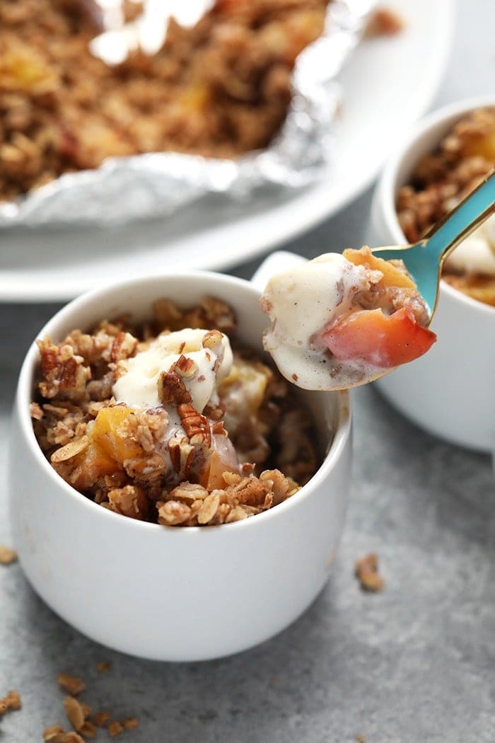 Peach season is here and this foil-pack peach crumble recipe on the grill is easy, delicious, and healthy! It's made with juicy peaches tossed in maple syrup and a yummy crumble topping, making it a gluten free fruit crumble and a healthy dessert recipe for the summertime! Peach crumble in coffee mug with spoon.