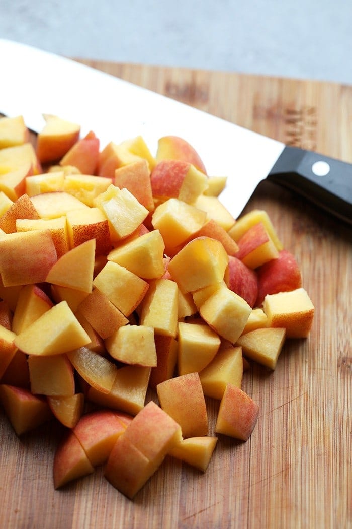 Dessert never tasted so good with this incredible foil pack peach crisp recipe! Made with juicy peaches and a simple crumble topping this summer dessert is healthy and delicious. Sliced peaches on cutting board.