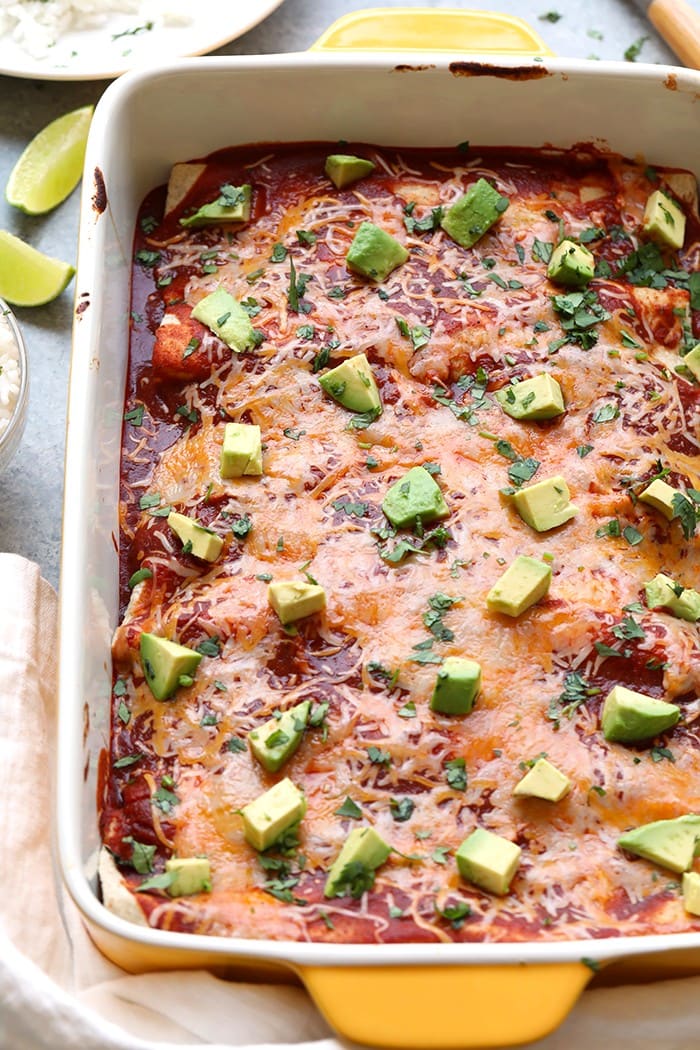 baking dish full of healthy chicken enchiladas topped with melted cheese and avocado