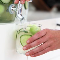 A person pouring cucumber-infused water into a glass.