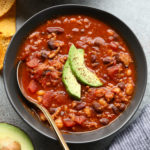 A bowl of chili with avocado and tortilla chips.