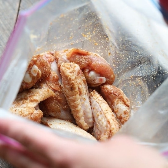 a person is placing baked chicken wings in a plastic bag.