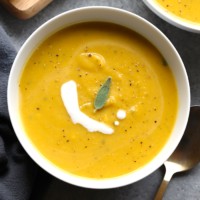 Two bowls of butternut squash soup with sour cream and sage.