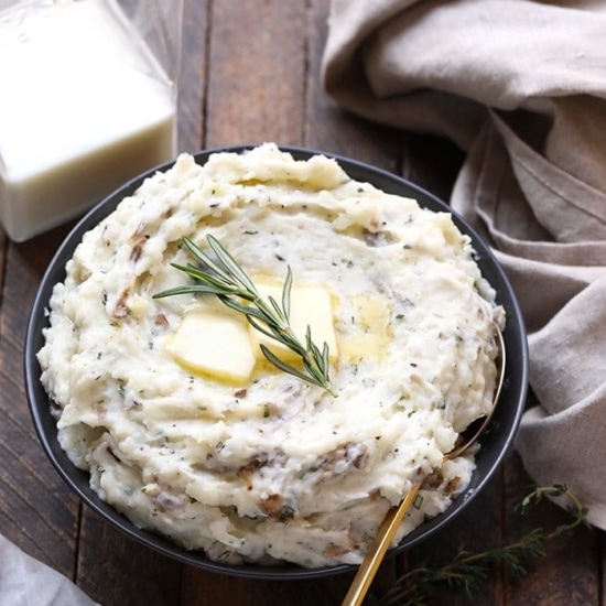 a bowl of healthy mashed potatoes with butter and sprigs of rosemary.