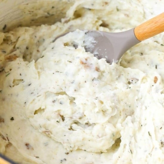 Healthy mashed potatoes made in a yellow pot with a wooden spoon.