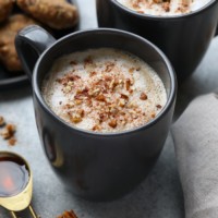 DIY maple pecan latte with whipped cream and pecans served in two black mugs.