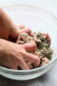 A person effortlessly combines herbs and meat in a bowl to create a delectable dish.