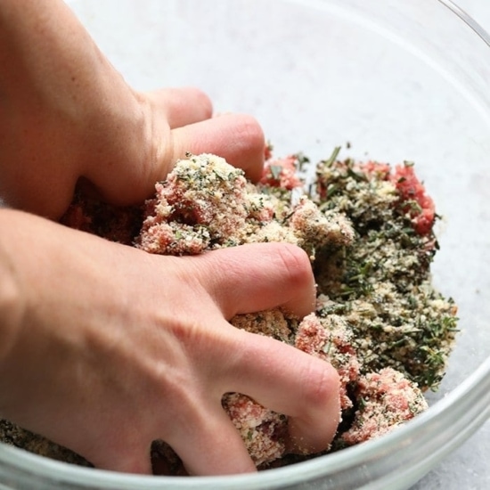 A person effortlessly combines herbs and meat in a bowl to create a delectable dish.