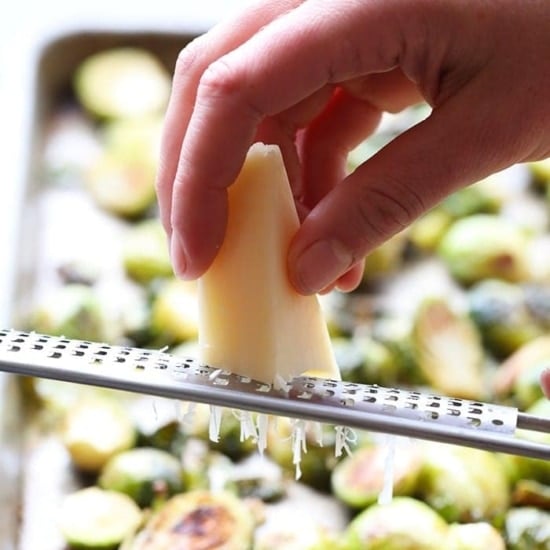 a person grating parmesan on roasted brussel sprouts.