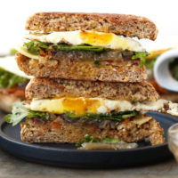 A breakfast sandwich stack with a fried egg atop toasted bread slices.