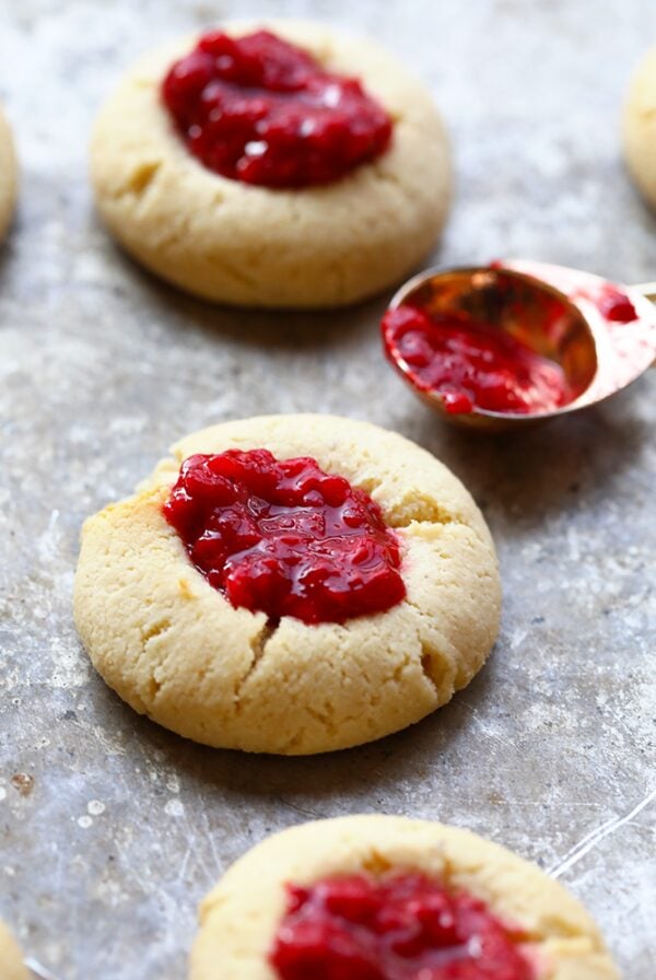 Raspberry thumbprint cookies filled with a spoon of cranberry sauce.