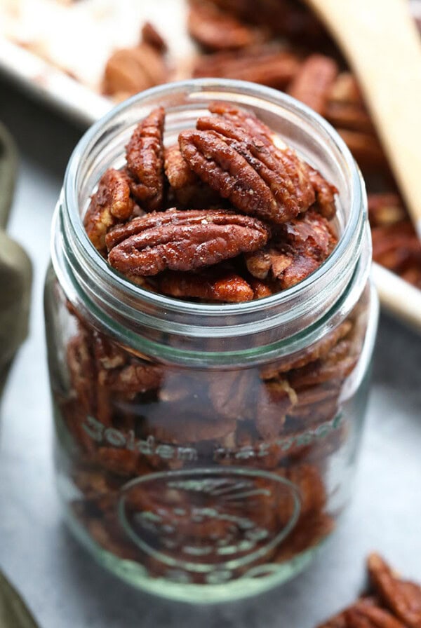 Roasted pecans displayed in a glass jar on a table.