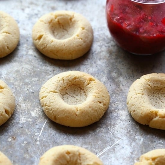 A tray of Raspberry Thumbprint Cookies on a baking sheet with a jar of jam.